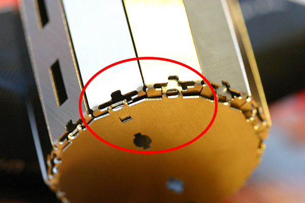 専用の冶具と手だけで組立てられるよう、随所に工夫が凝らされている。写真はロボットの胴体の底部分。底パーツをはめただけ(赤枠内右側)だとすぐ取れてしまうので、冶具の先端で底パーツのツメを内側に押し込み、引っ掛けて固定する(左側)